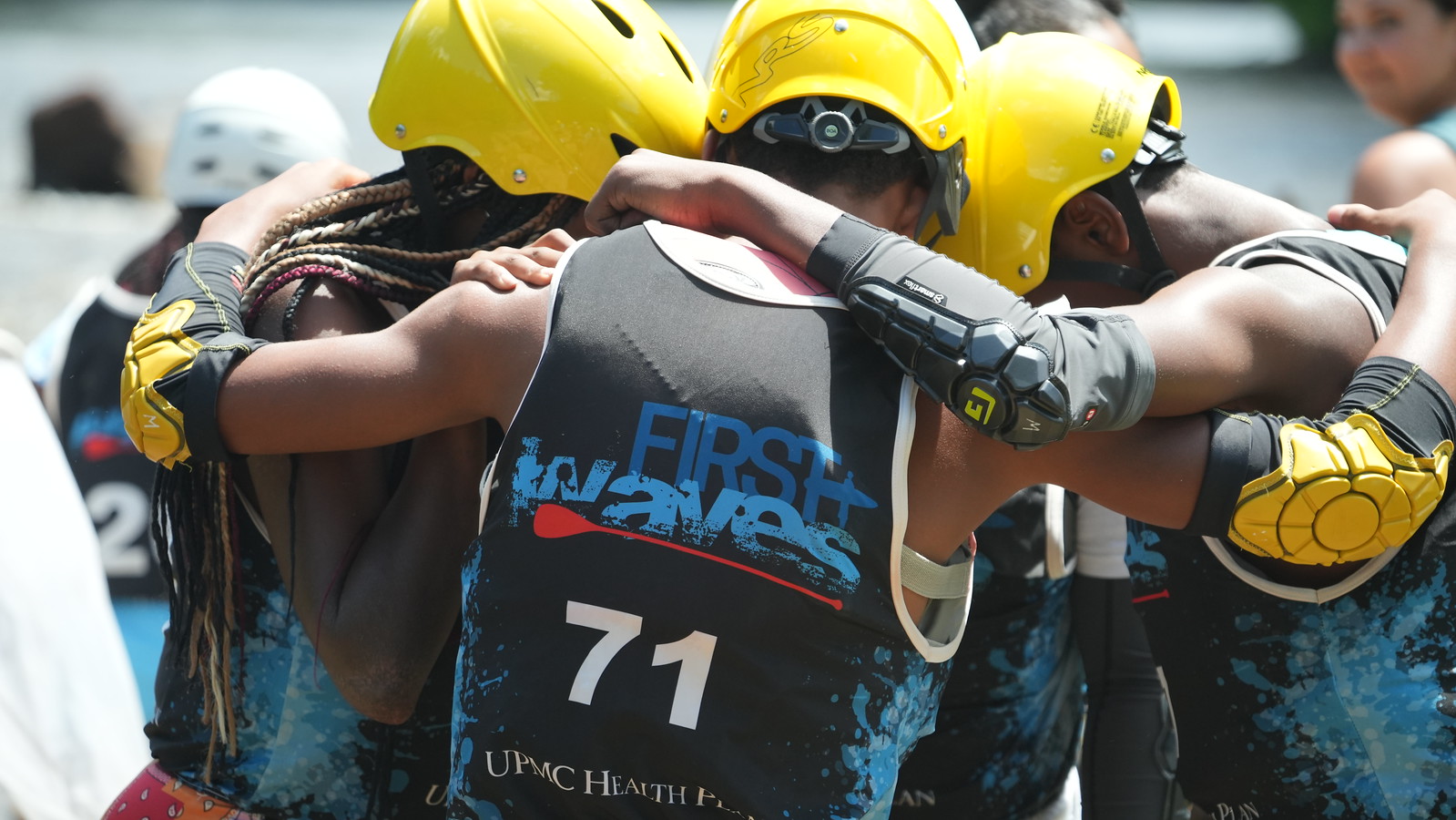 A group of young people in helmets and PFDs stand with their arms around each other