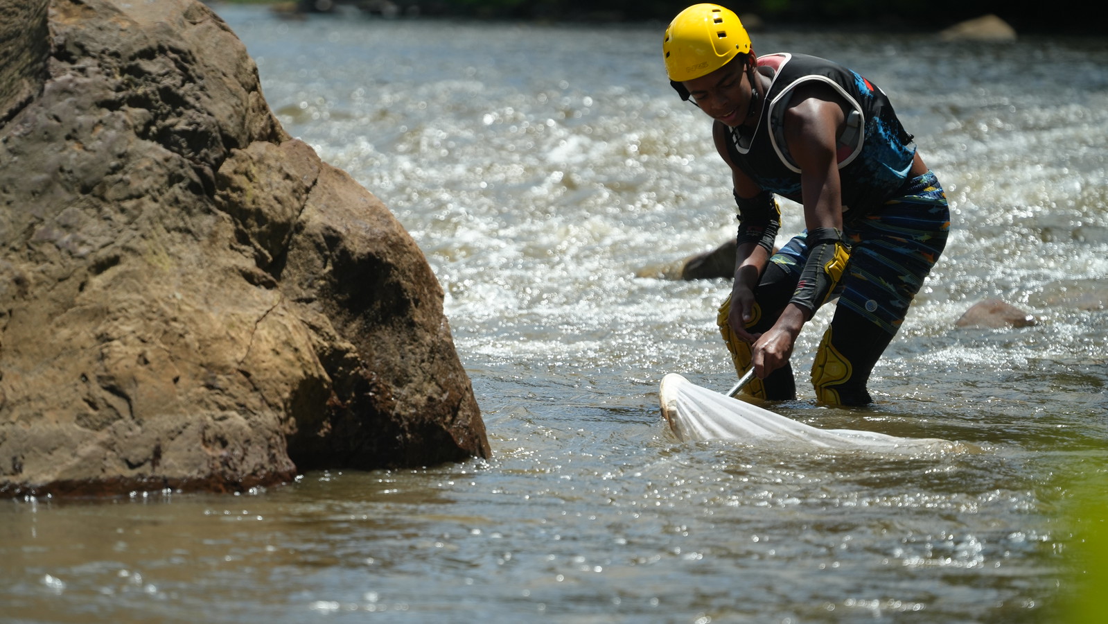 A young person stands in a river holding a net in the water