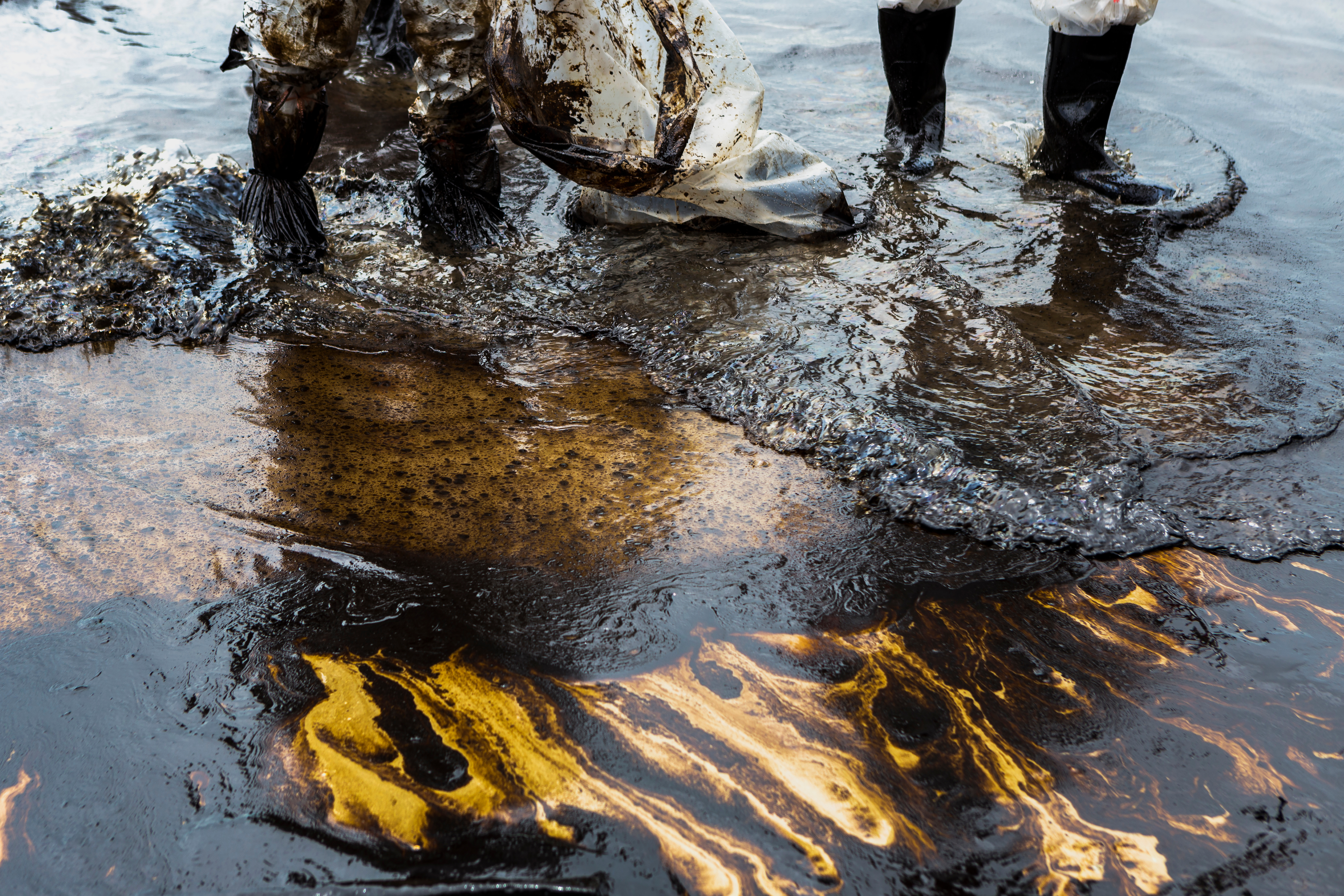 people in boots stand in water polluted with oil