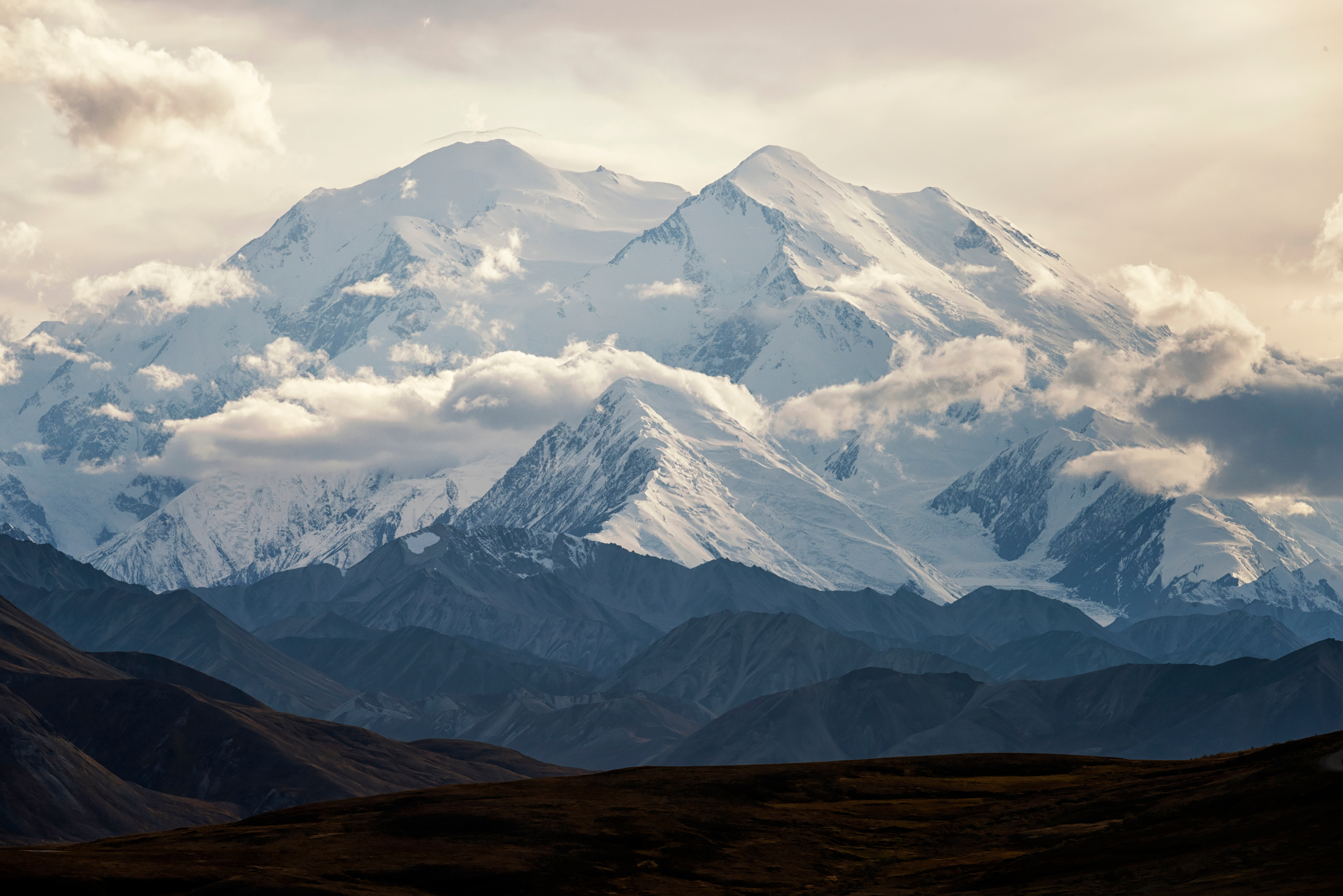 A large snowy mountain with clouds above it