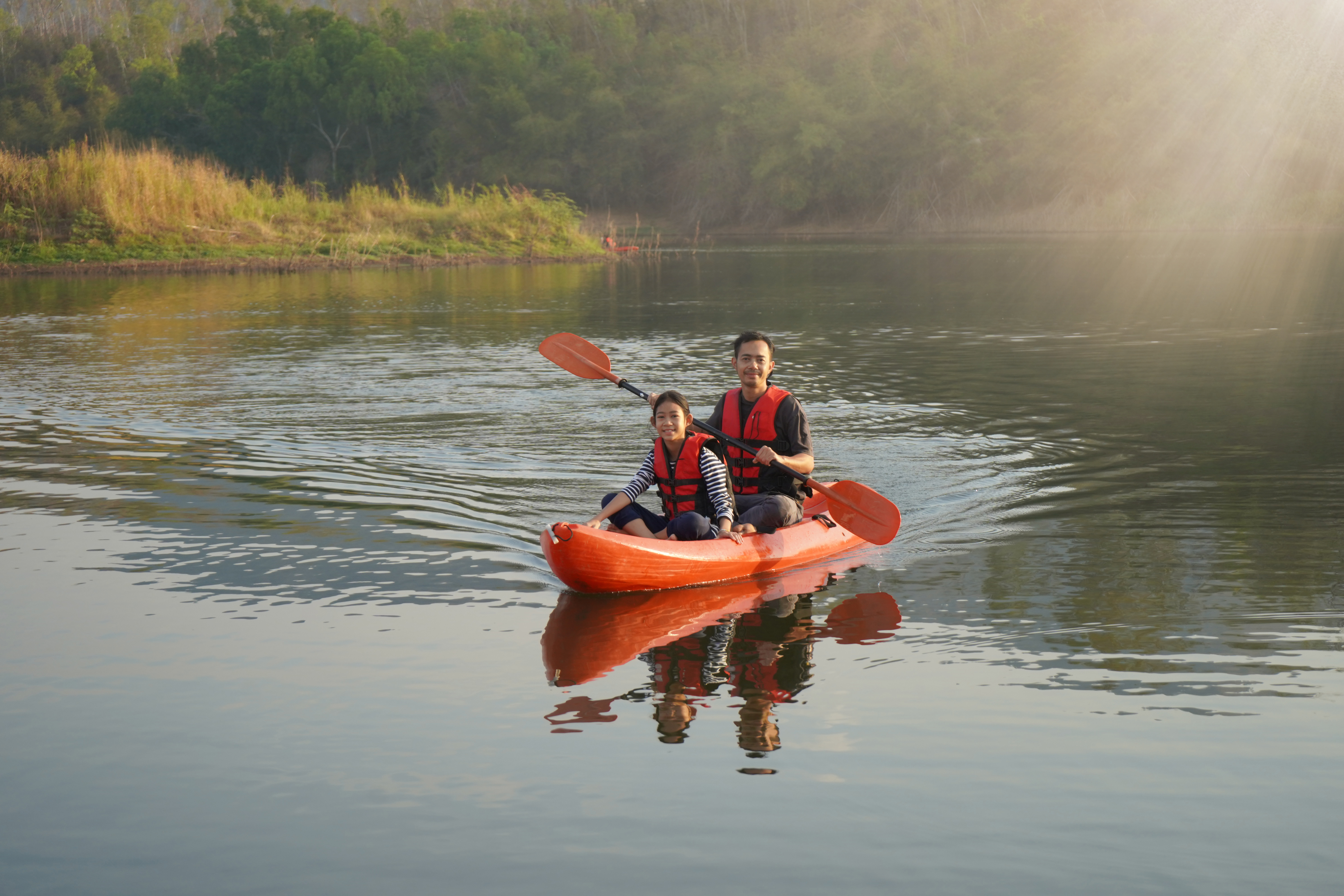 An adult and child paddle a boat across a lake