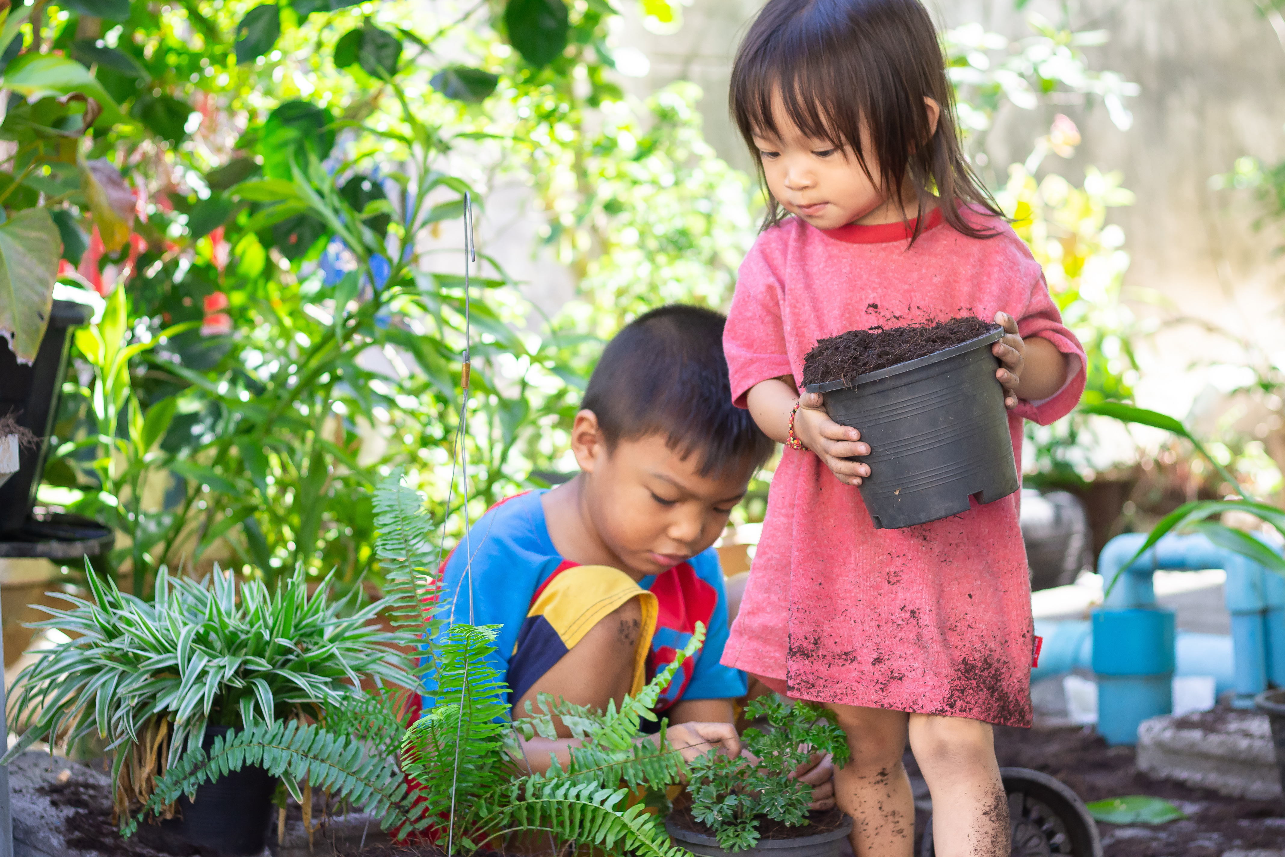 two children crouch in the dirt, one of them holding a plant pot