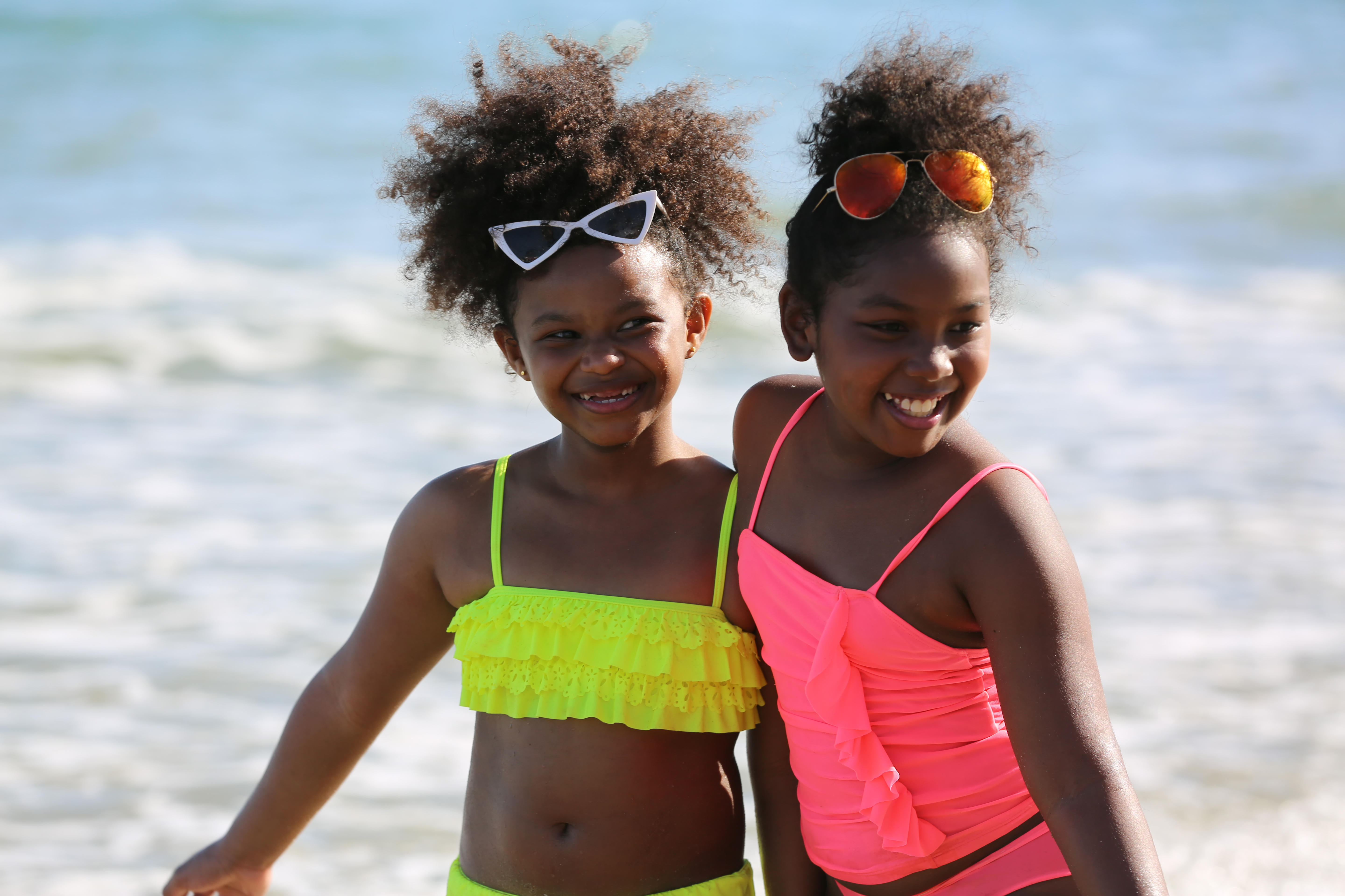 Two girls smile at the beach while wearing brightly colored bathing suits