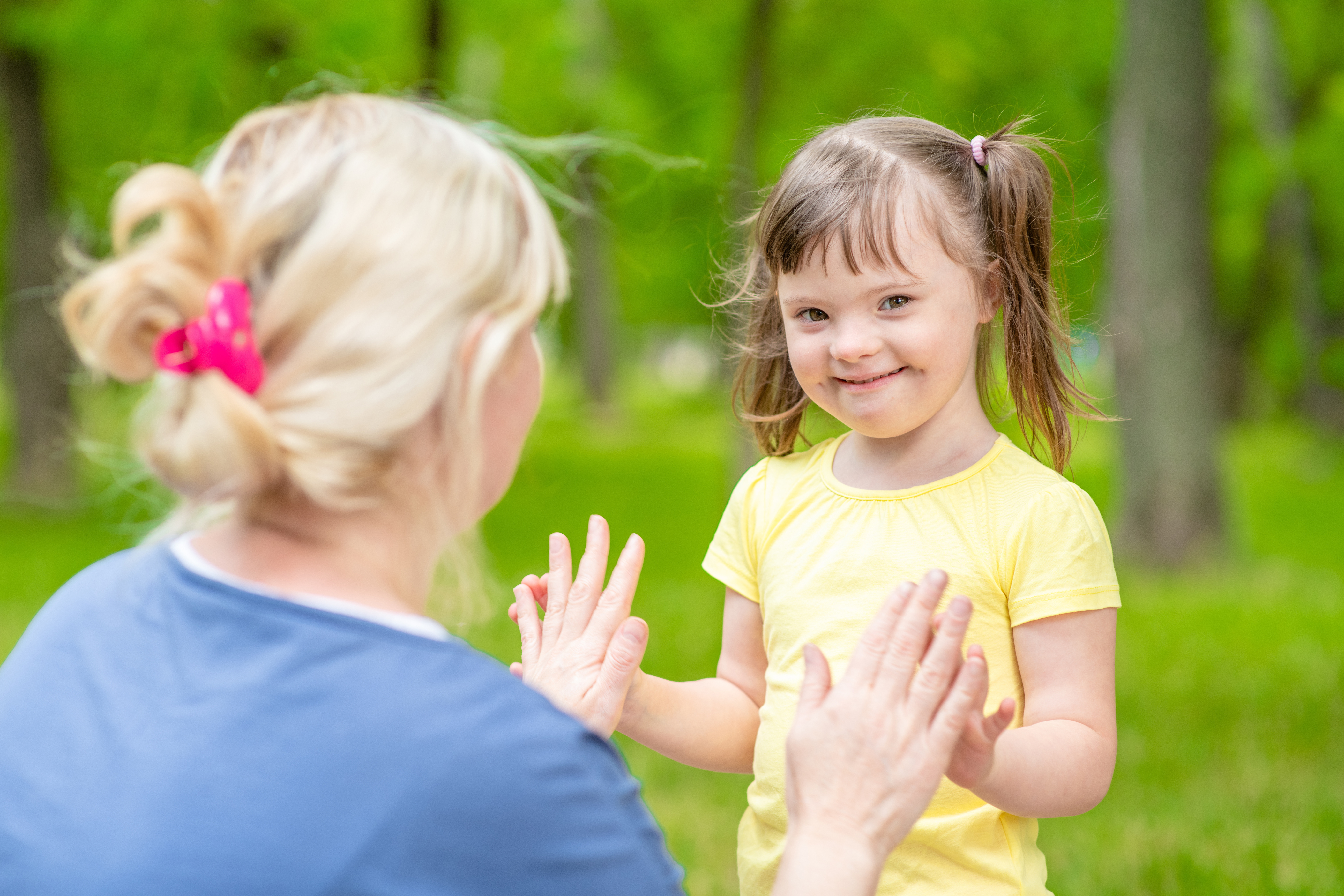 An adult and child touch hands while standing near trees