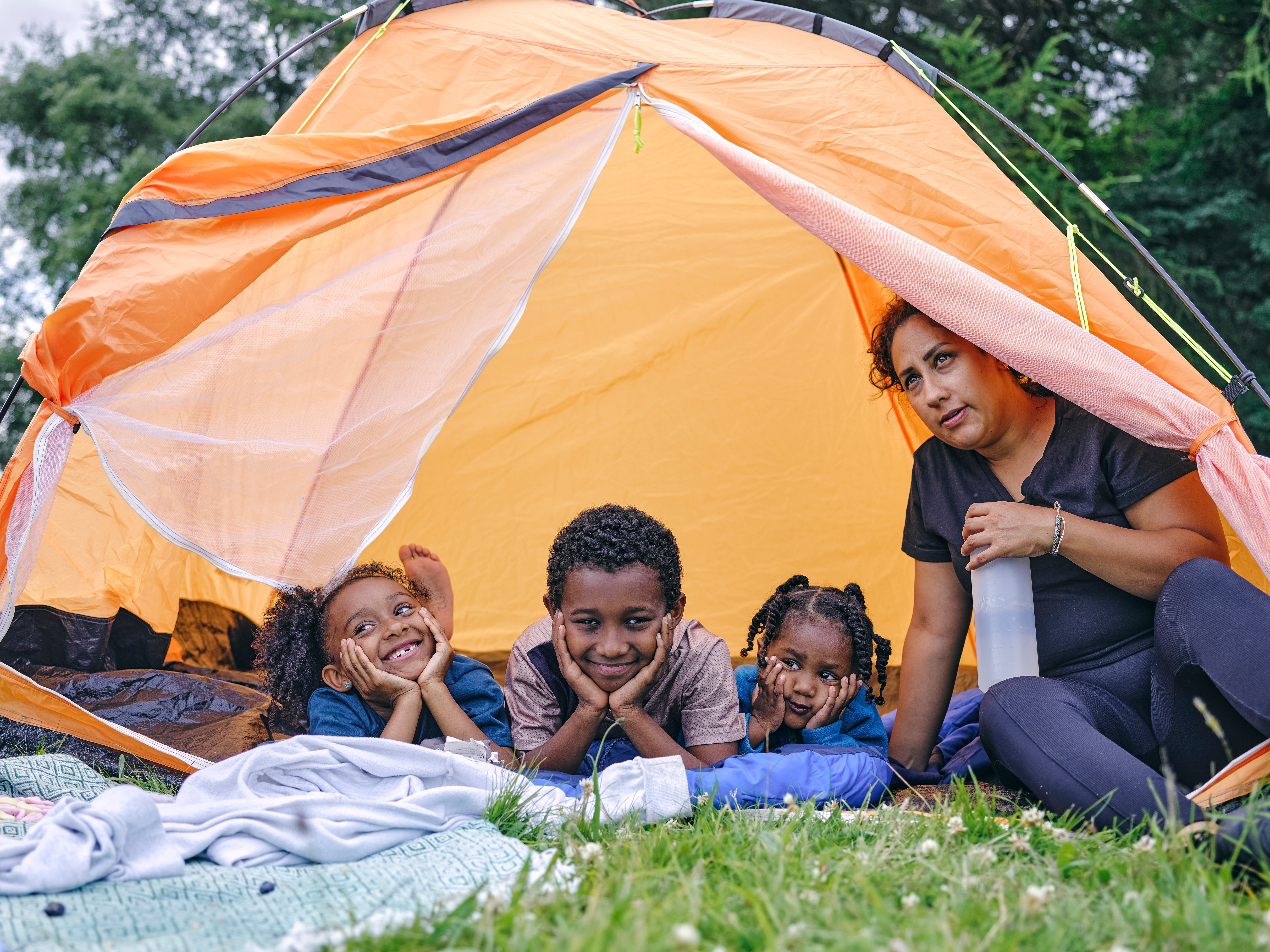 An adult and three kids smile from inside a tent