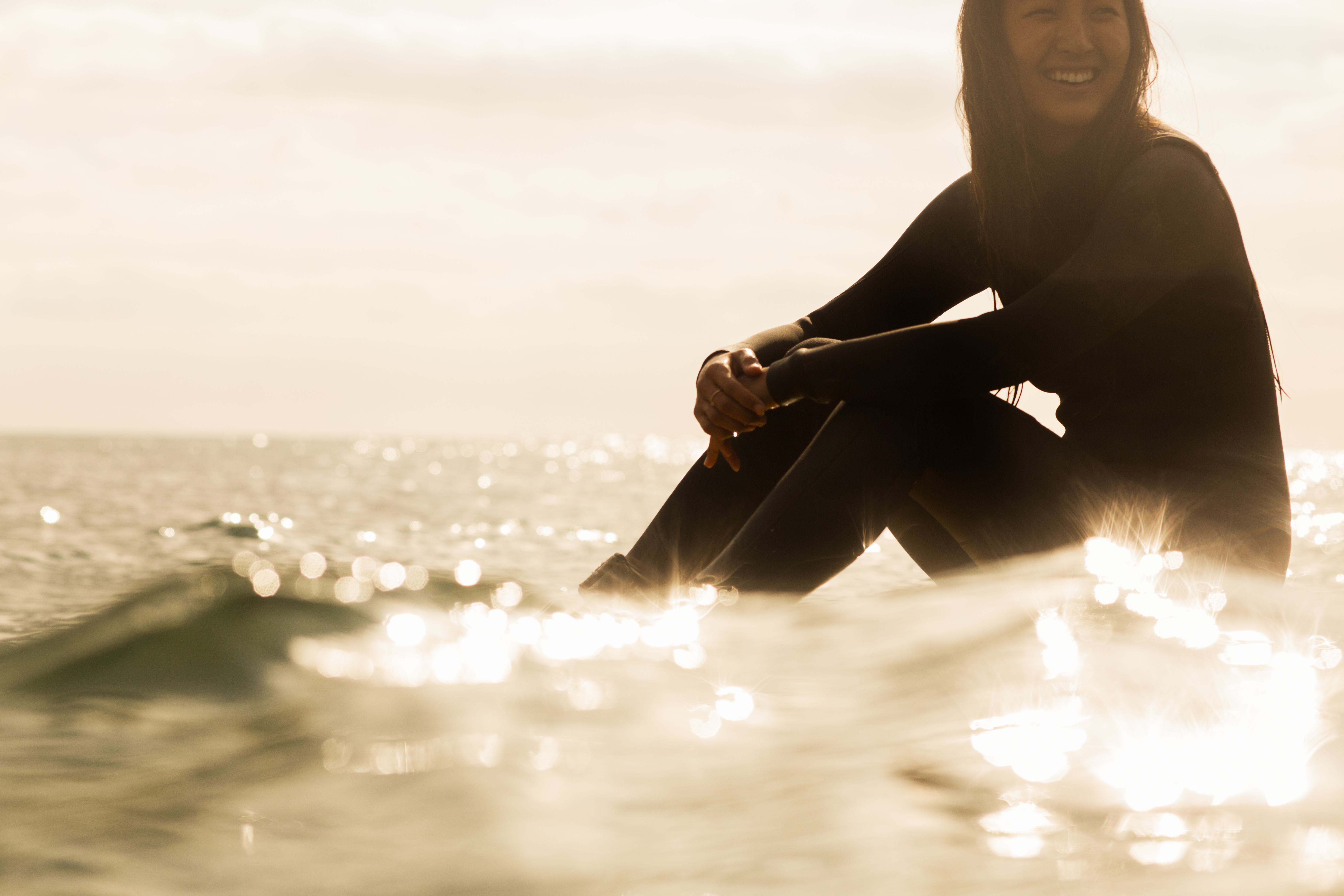 A young person sits in the ocean on a surf board