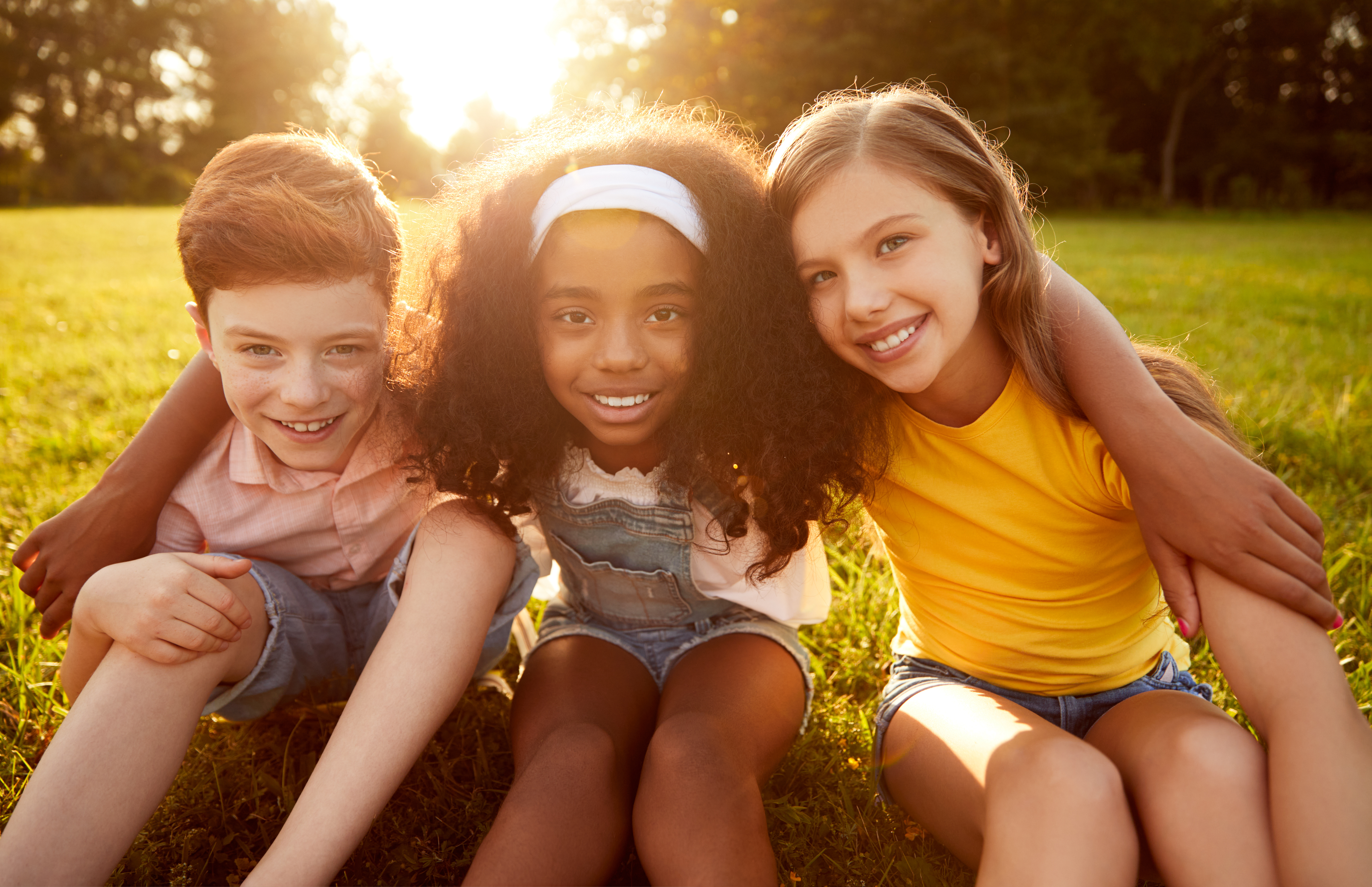 Three young people sit in grass with arms around each other