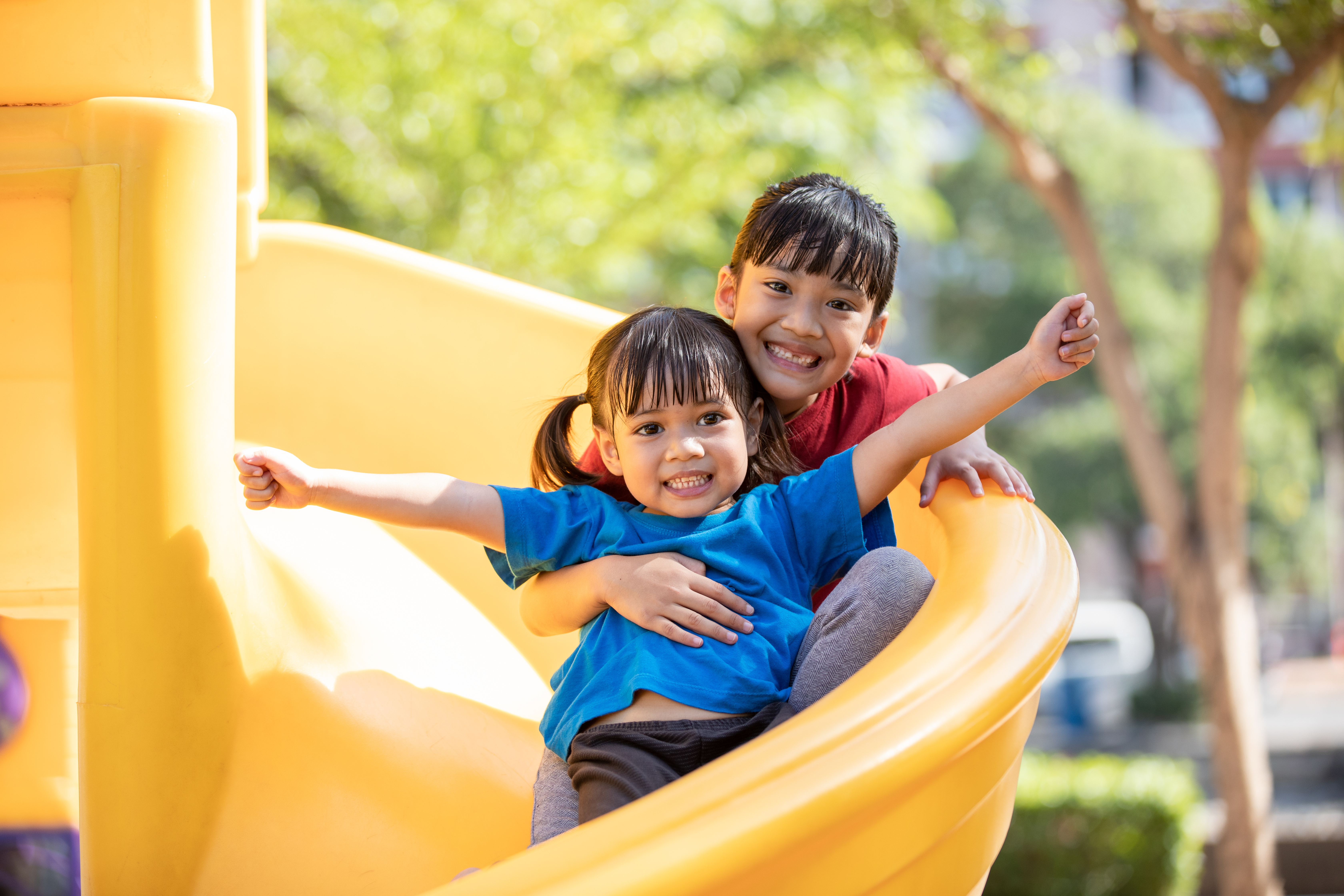 Two kids smile while sitting on a slide together