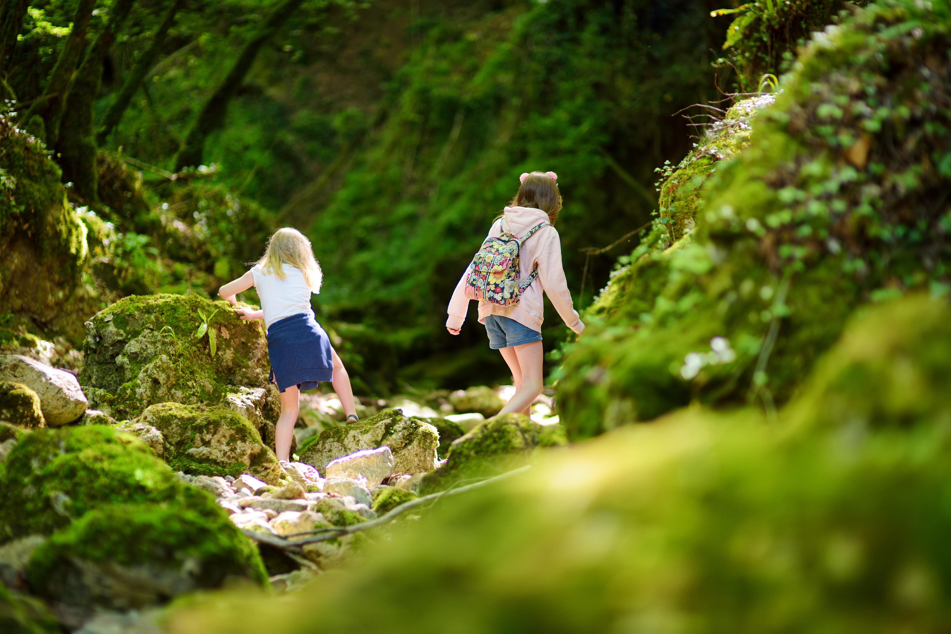 Two kids climb over moss covered rocks