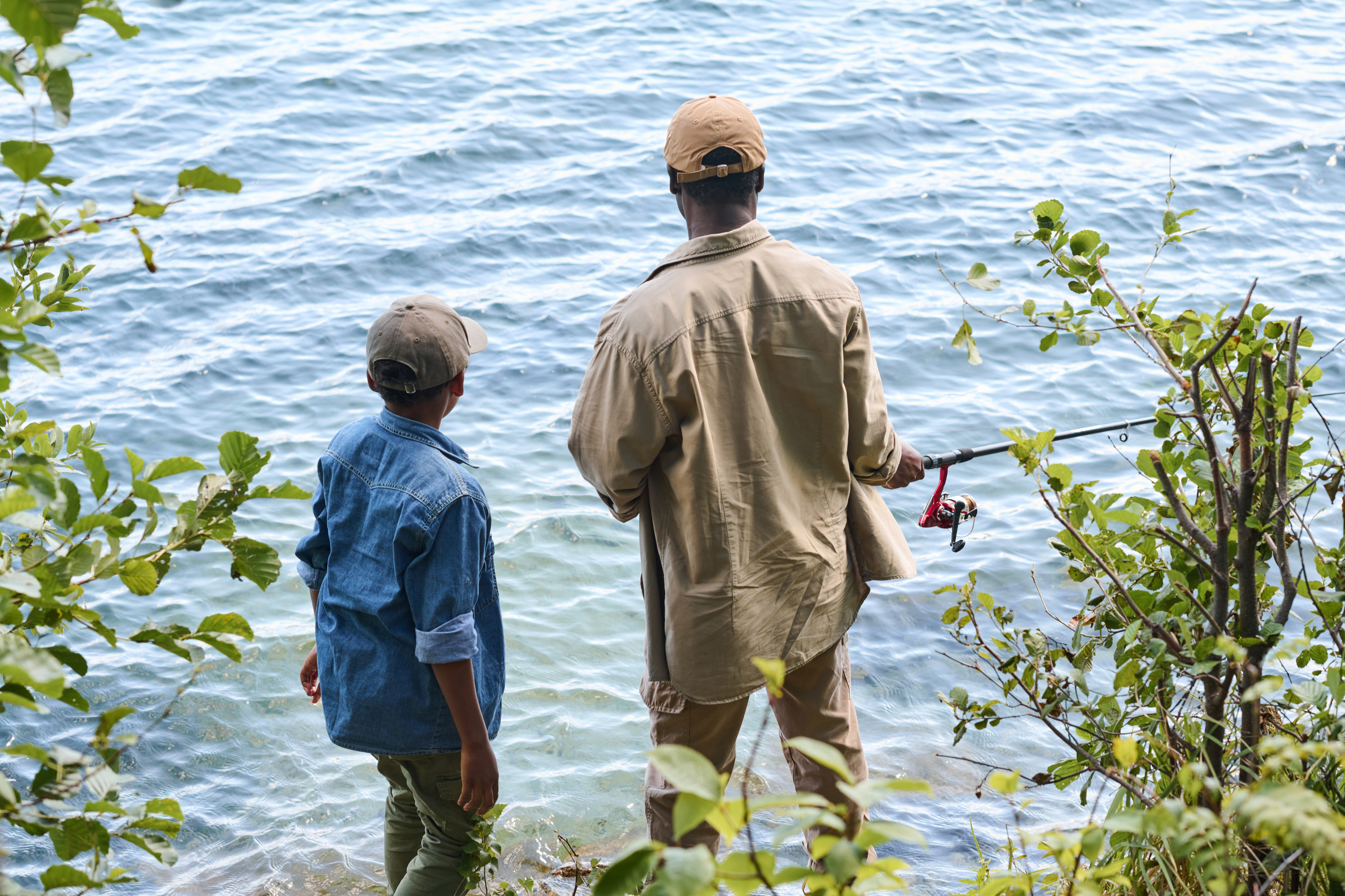 An adult and child stand lookin at water holding fishing poles