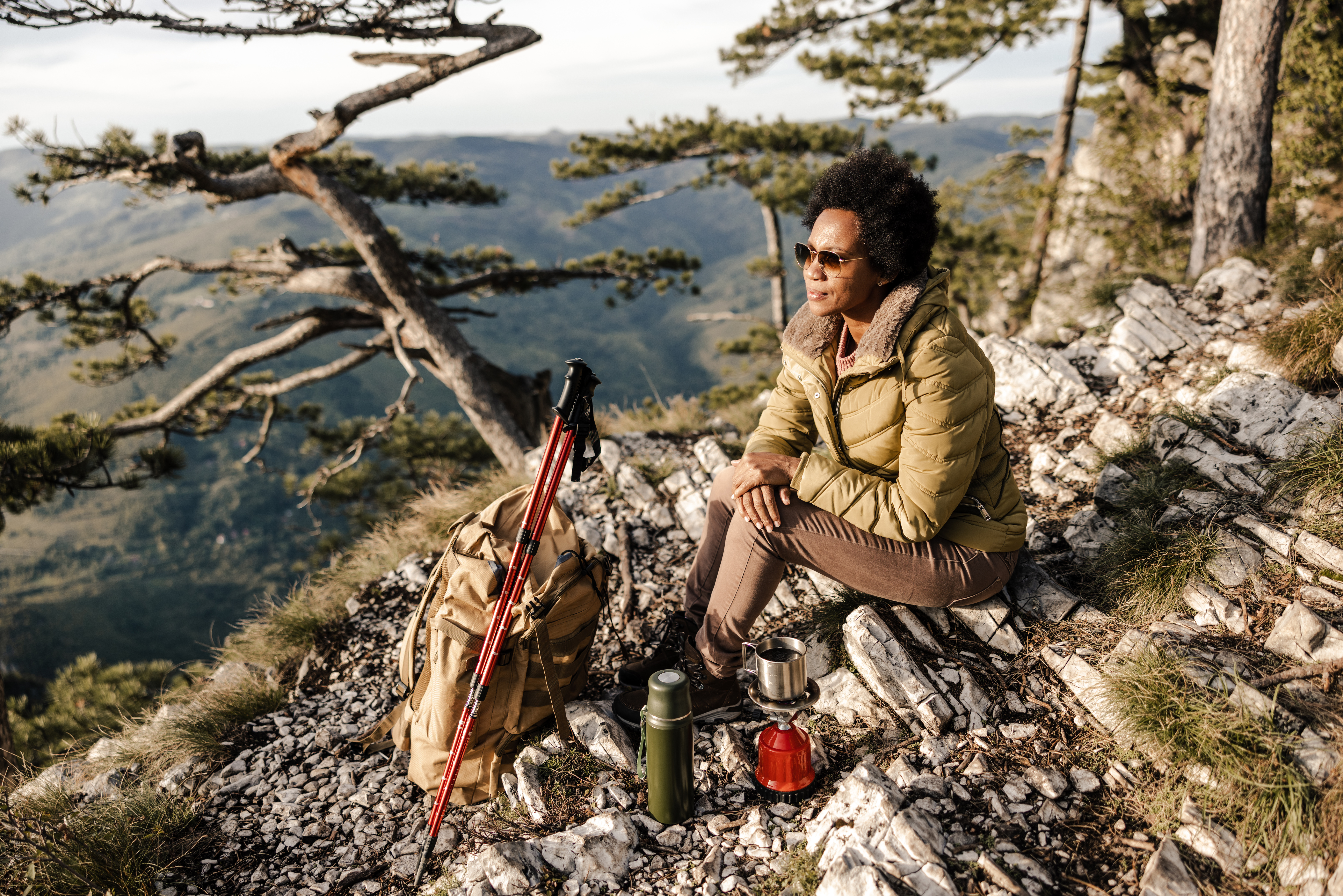 a person sits near a cliff edge with a backpack and a camp stove, looking at the view