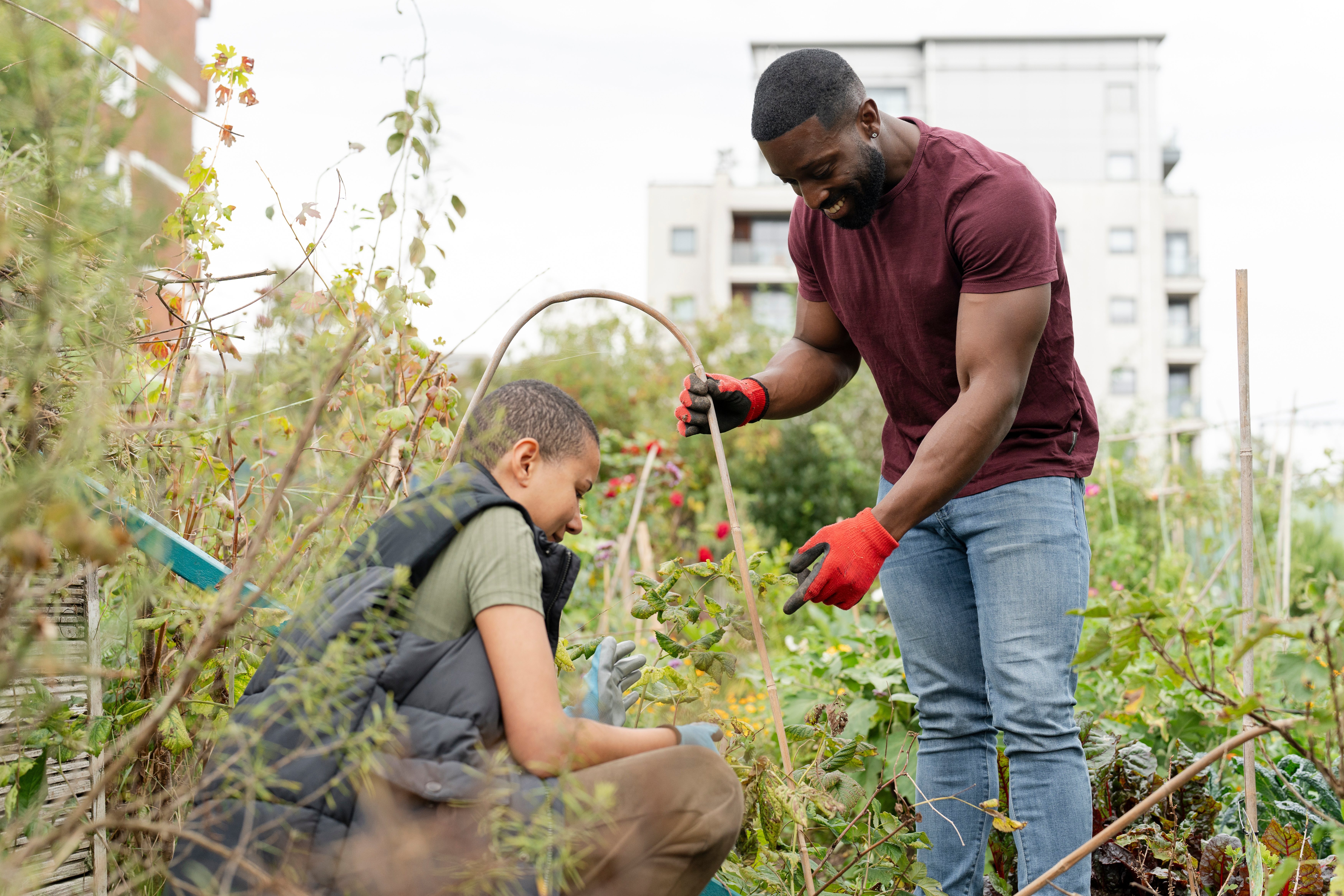 Two people work in a garden with tall buildings around them