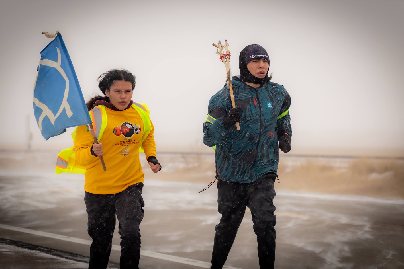 Two teenagers run through the snow next to each other