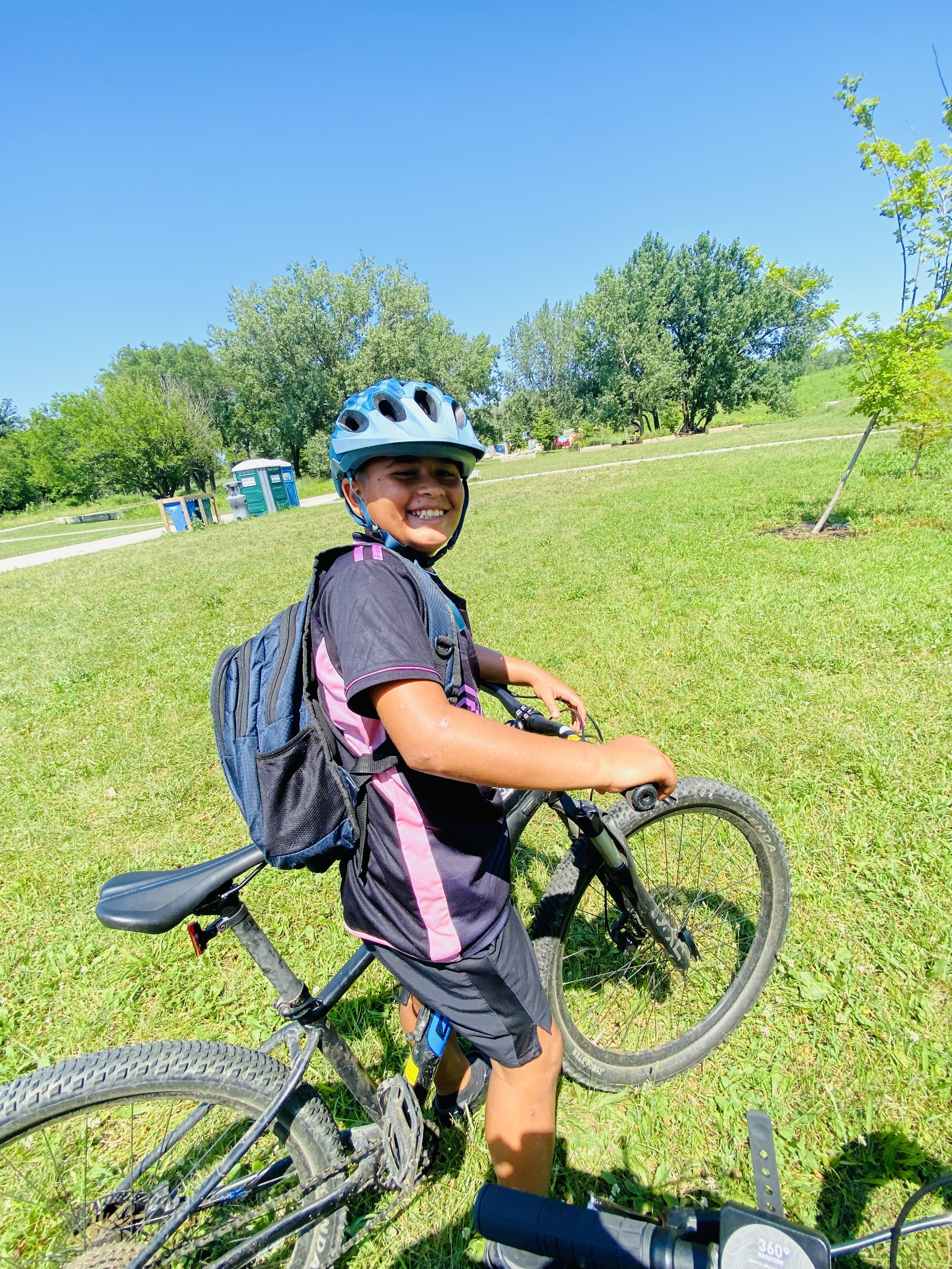 A young person stands over a mountain bike and smiles